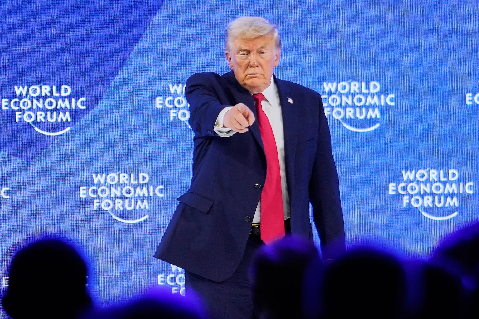 A man in suit and tie points his finger at a crowd while on stage.
