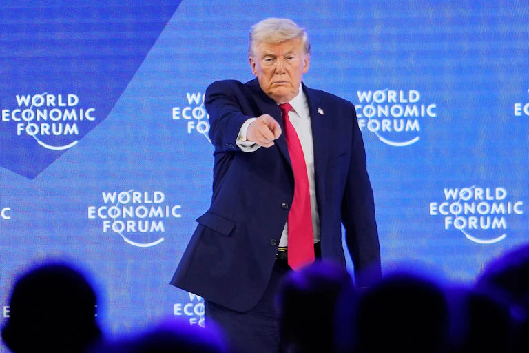 A man in suit and tie points his finger at a crowd while on stage.