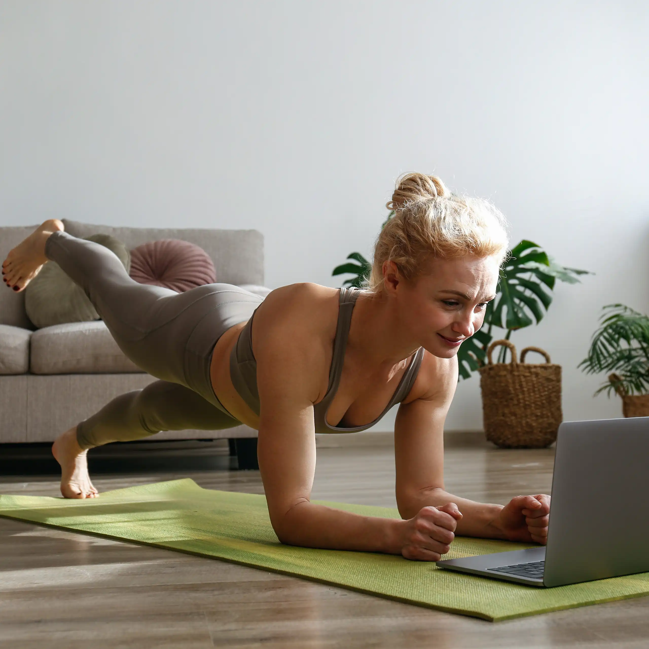 Uma mulher faz exercícios no chão da própria casa, olhando para um laptop