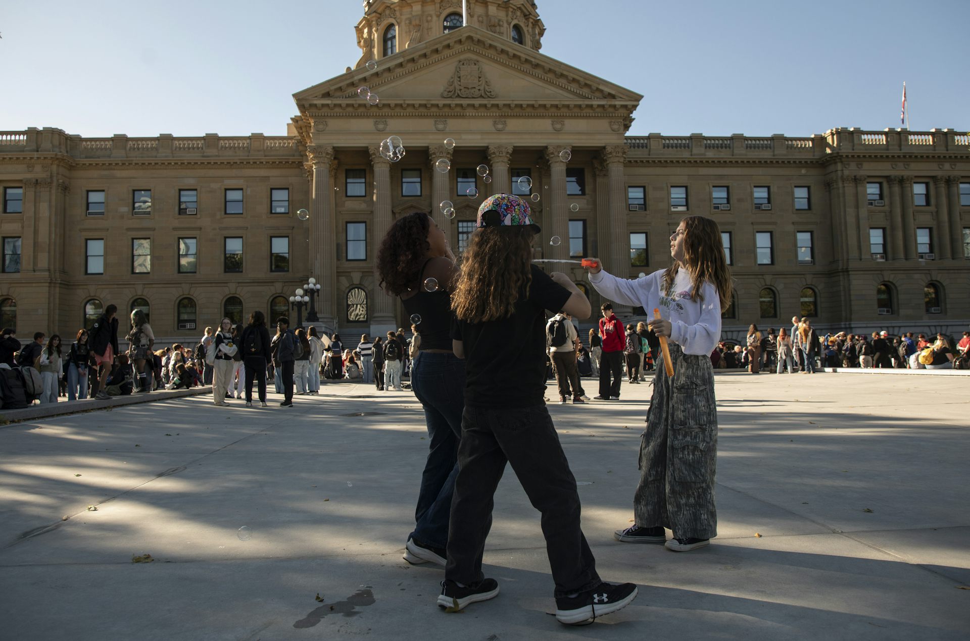 Students stand in front of a stone legislative building blowing bubbles.