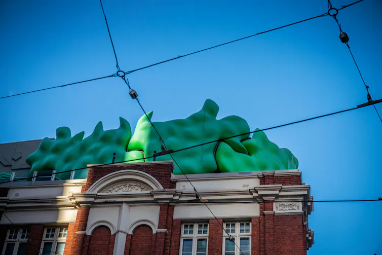 An old red brick building with a green sculpture on its roof.