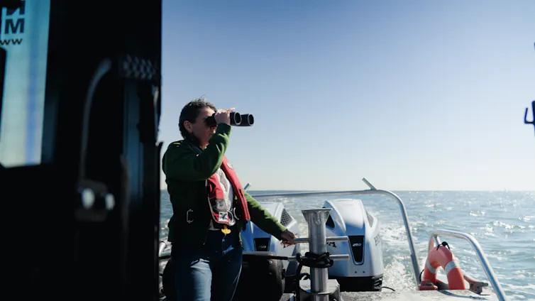 woman on boat, looks through binoculars at sea