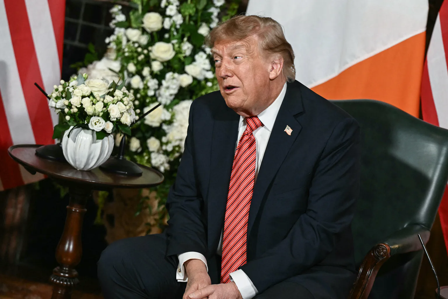 A man in a suit talks in front of a flag