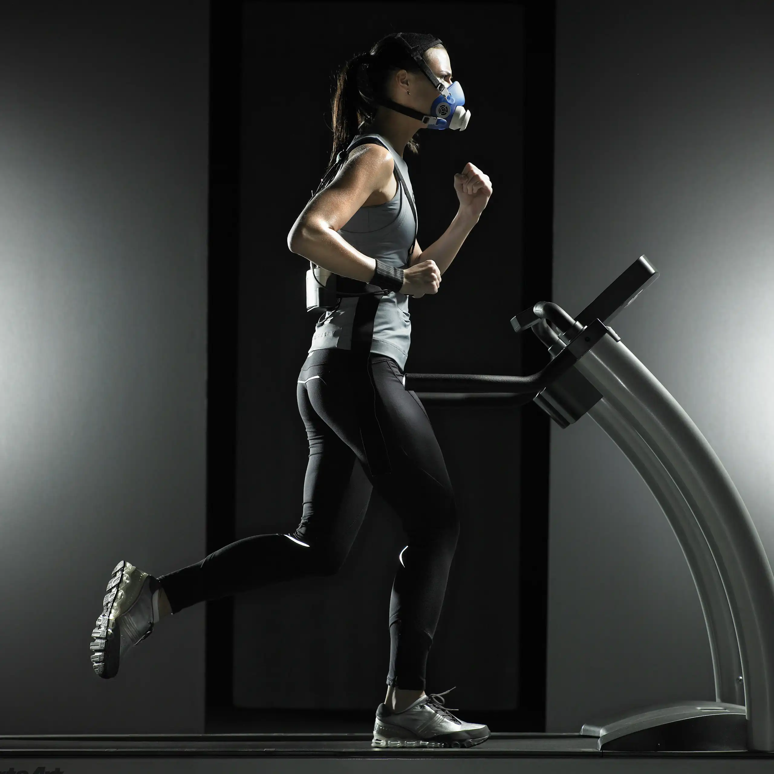 Une femme équipée d'un dispositif de mesure, en train de courir sur un tapis roulant