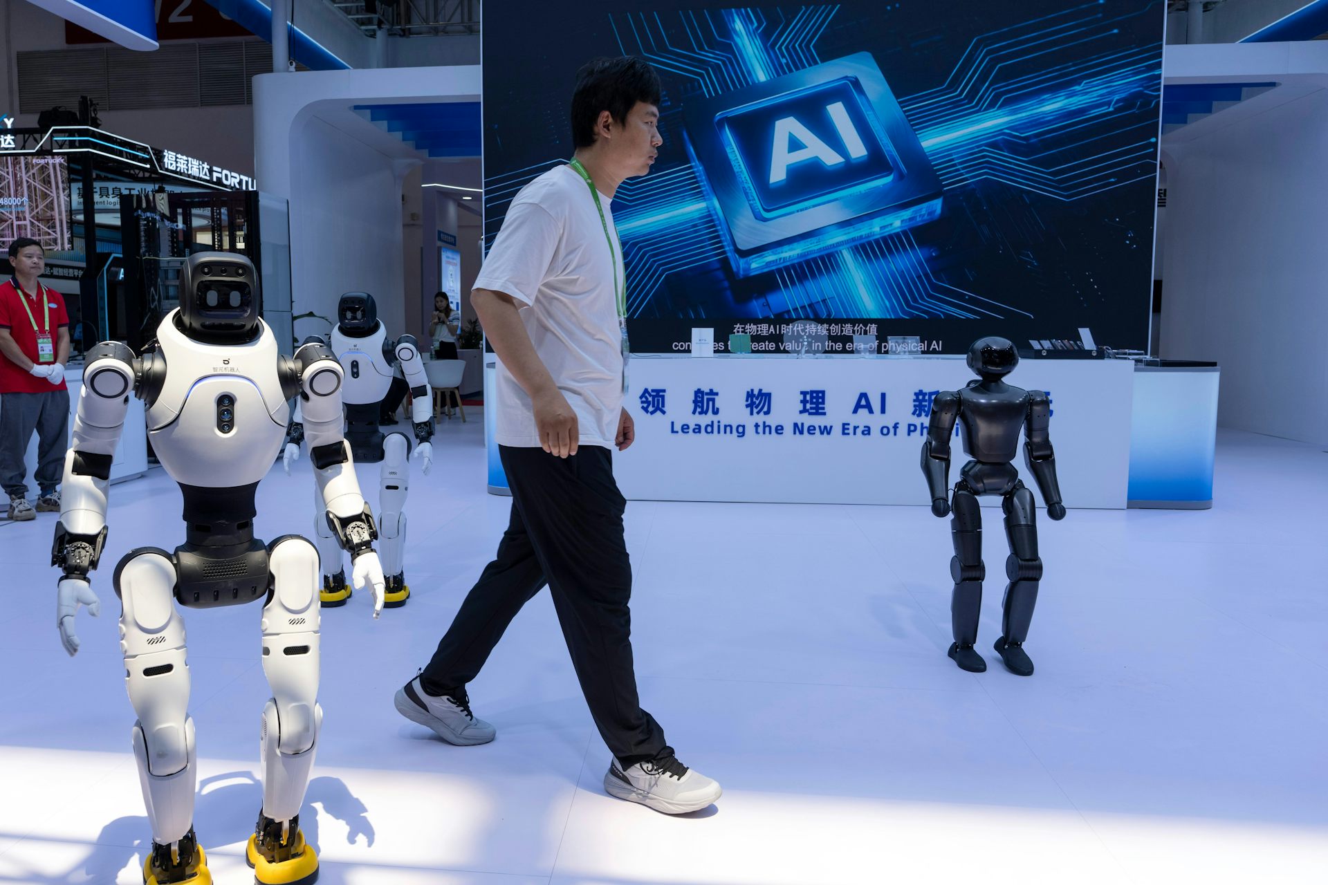 Un homme marche entre des robots humanoïdes, avec un panneau publicitaire faisant la promotion de l'IA en arrière-plan.