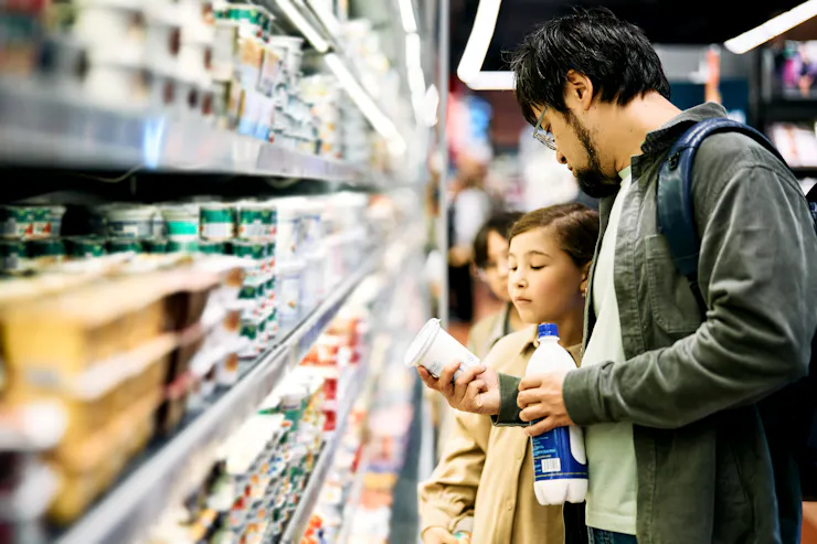 Adult and child in dairy aisle at grocery store examining a cup of yogurt
