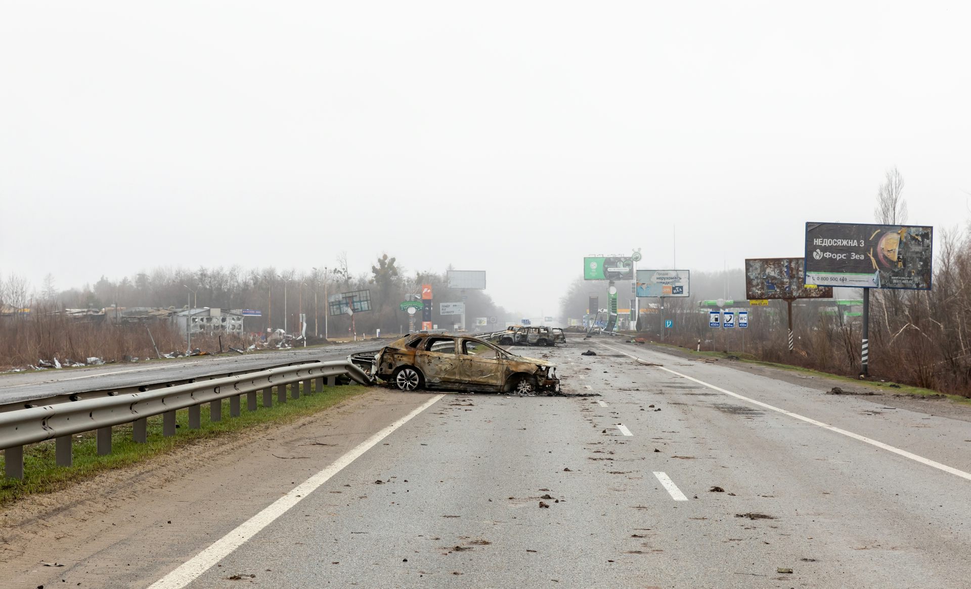 A destroyed car sits on the Zhytomyr highway on a foggy day.