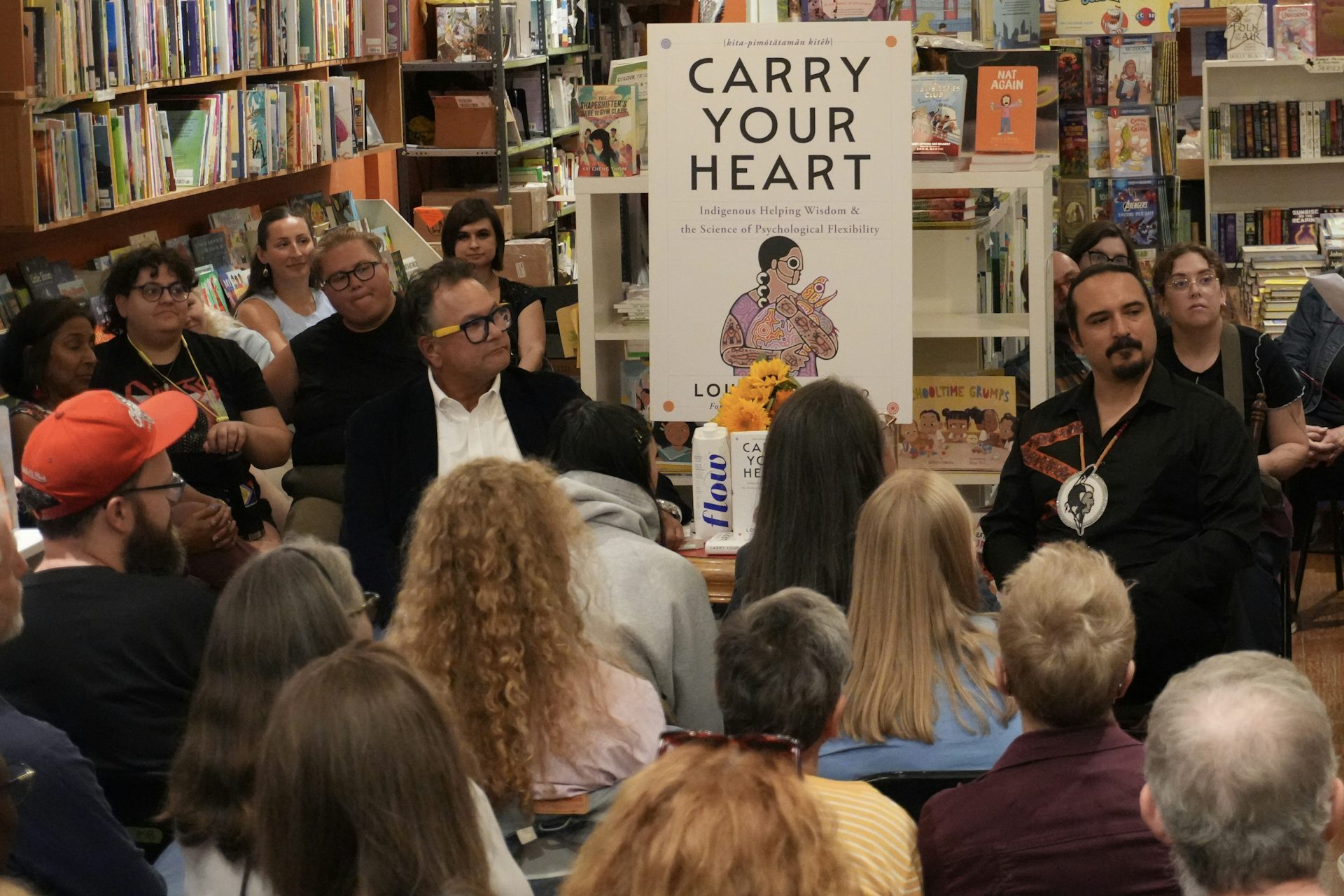 A room filled with an audience watching two men in conversation with a large scale version of a book cover behind them.