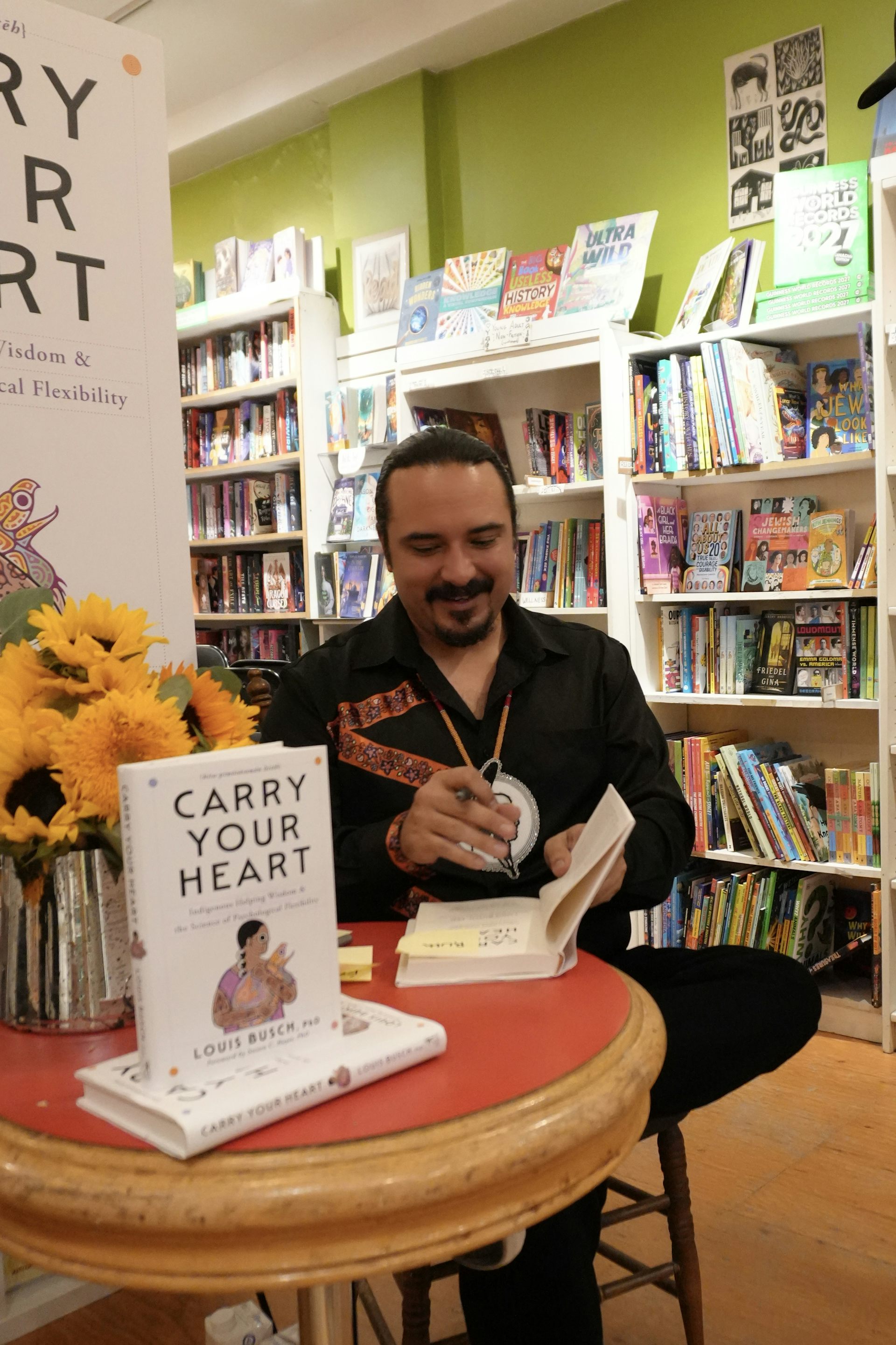 A man sitting at a small table signing books.