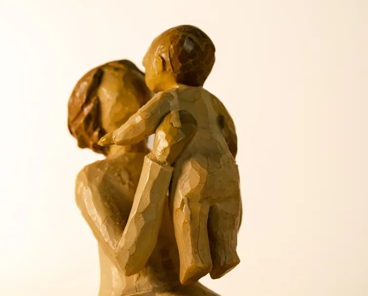 Wooden figure of a mother lifts up her baby to her face.