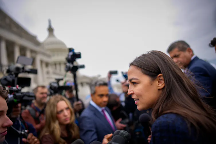 A dark-haired young woman being asked questions by reporters near the U.S. Capitol building.