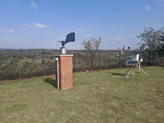 A small brick tower with a metal contraption on top with a kind of wing sticking out