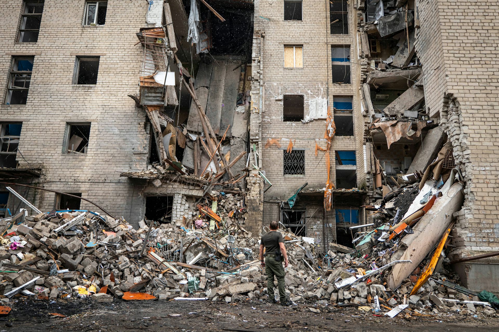 A tall residential apartment building partially damaged with a chunk missing from the middle and a large pile of debris at the bottom