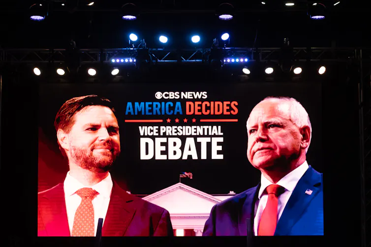 Two men, one shaded red and the other in a blue suit, seen on a TV screen.