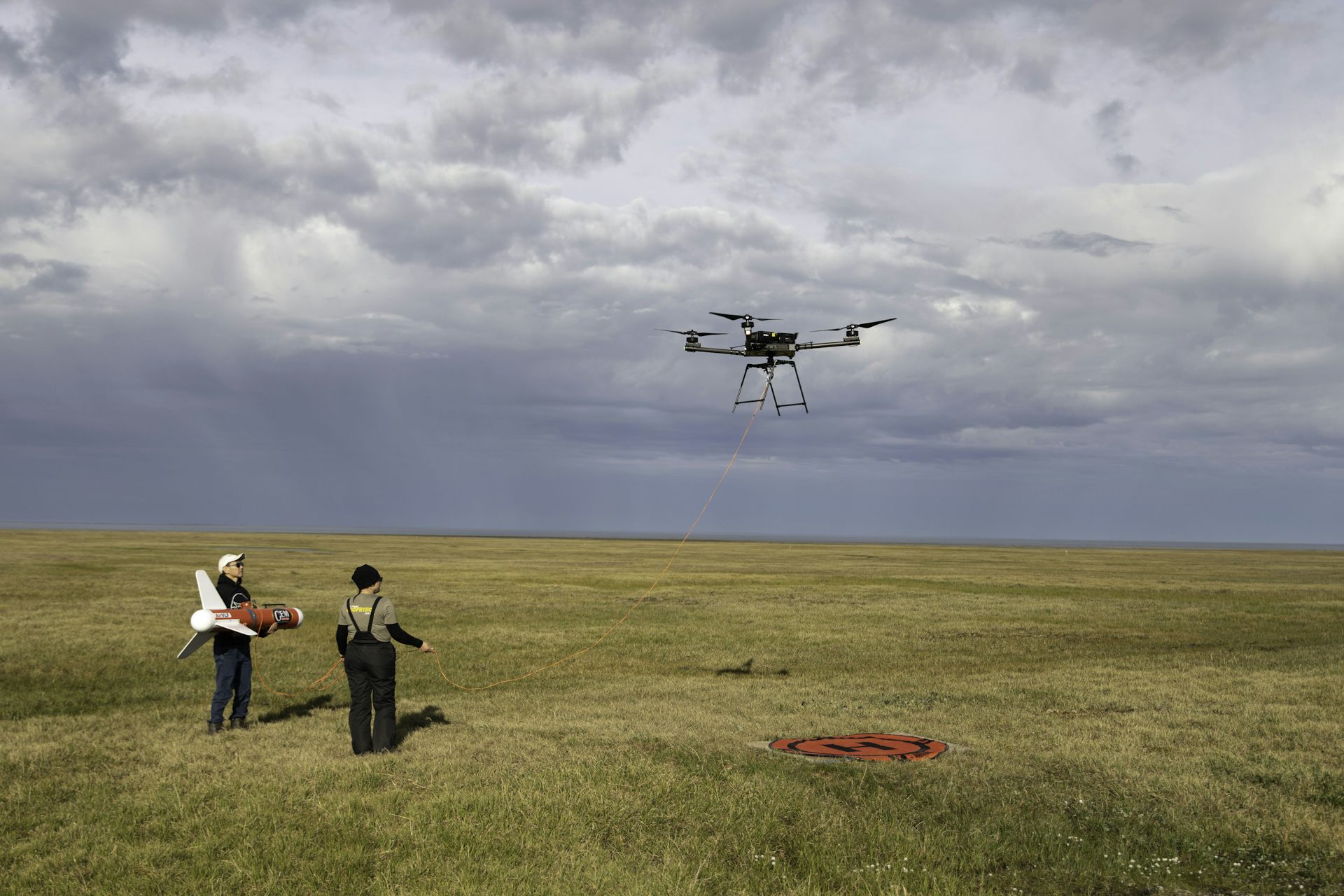 Two scientists operate a drone over a marshy area.