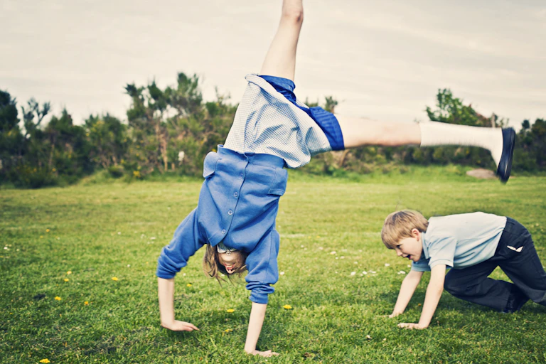 Two school children playing on grass, one child is doing a cartwheel.