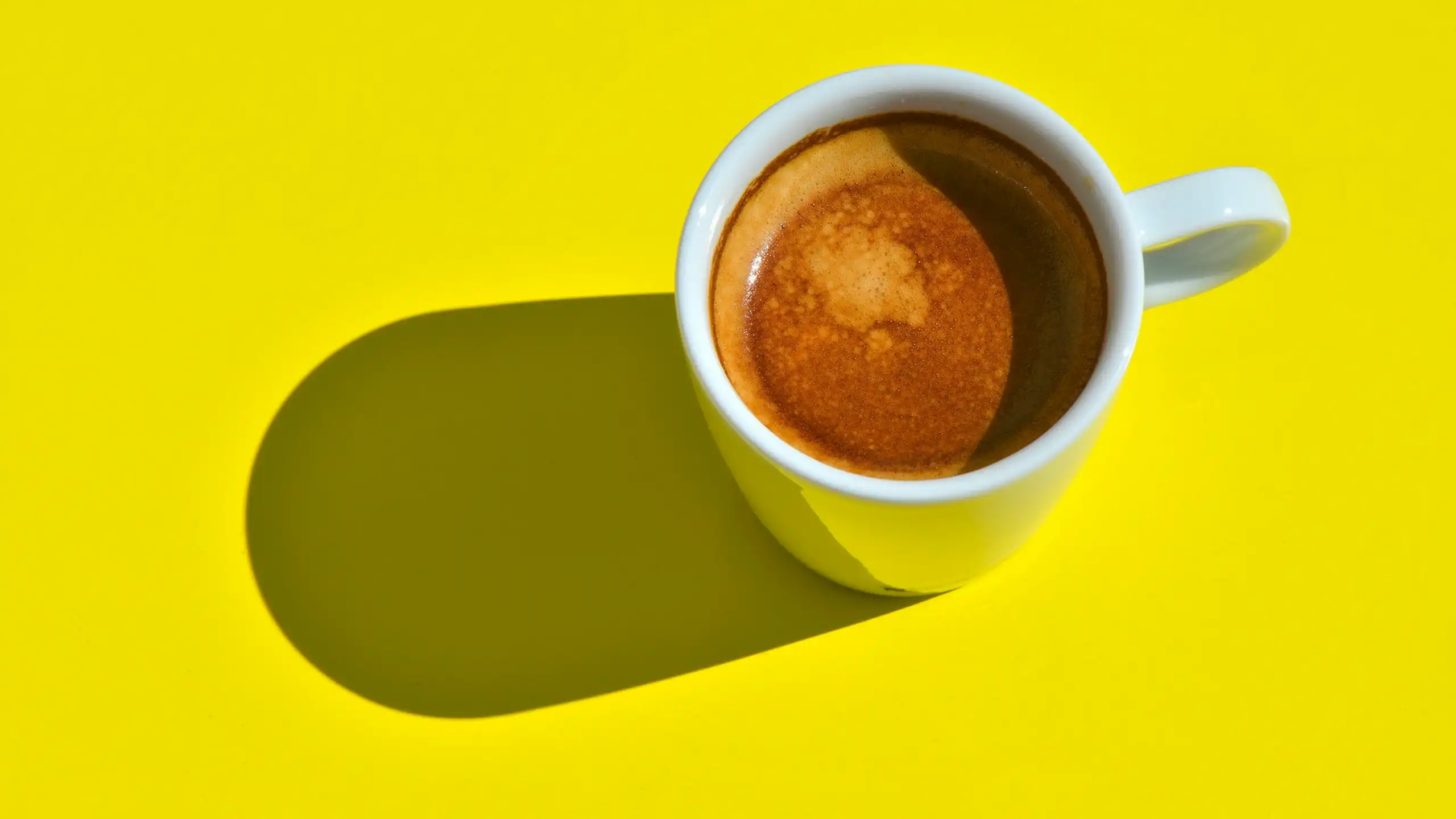 Cup of coffee in white mug or cup, viewed from above, against bright yellow background