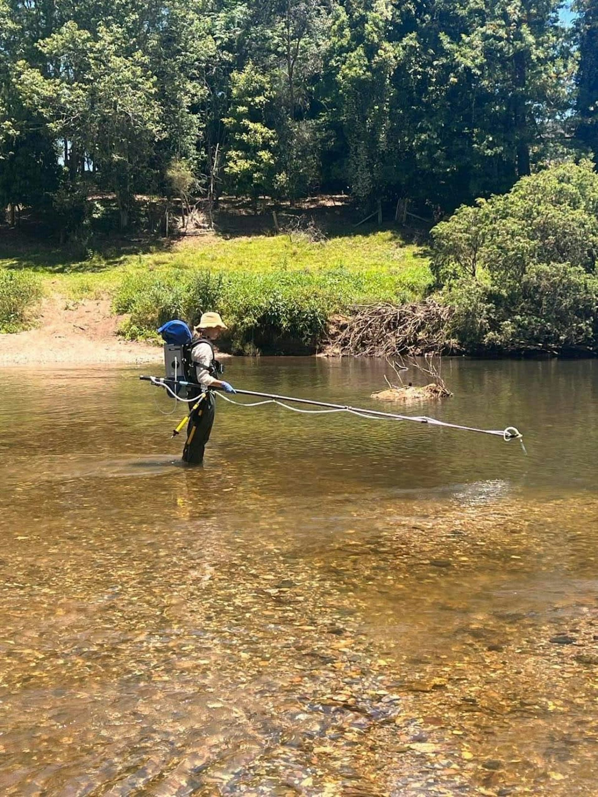 A researcher with a backpack samples collects water samples in a river.