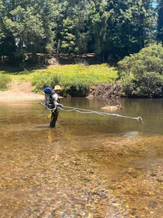A researcher with a backpack samples collects water samples in a river.
