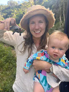 A woman and her baby smile while holding a baby turtle.