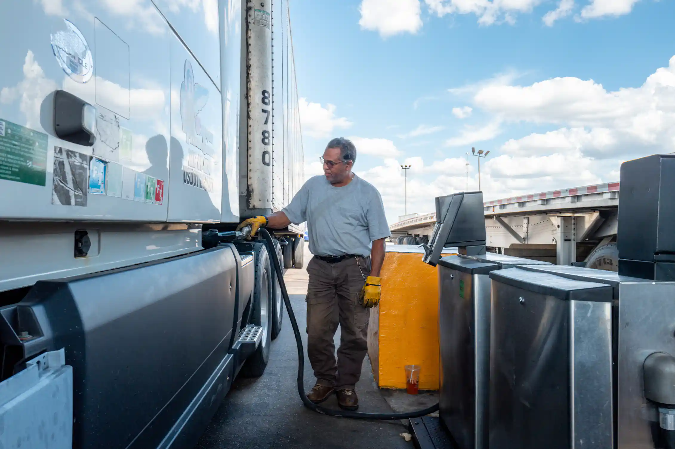 A person standing next to a large truck pumps fuel into a tank.