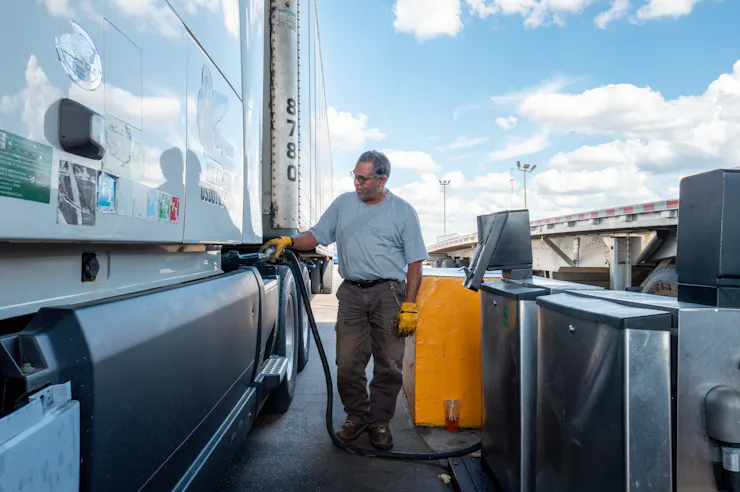A person standing next to a large truck pumps fuel into a tank.