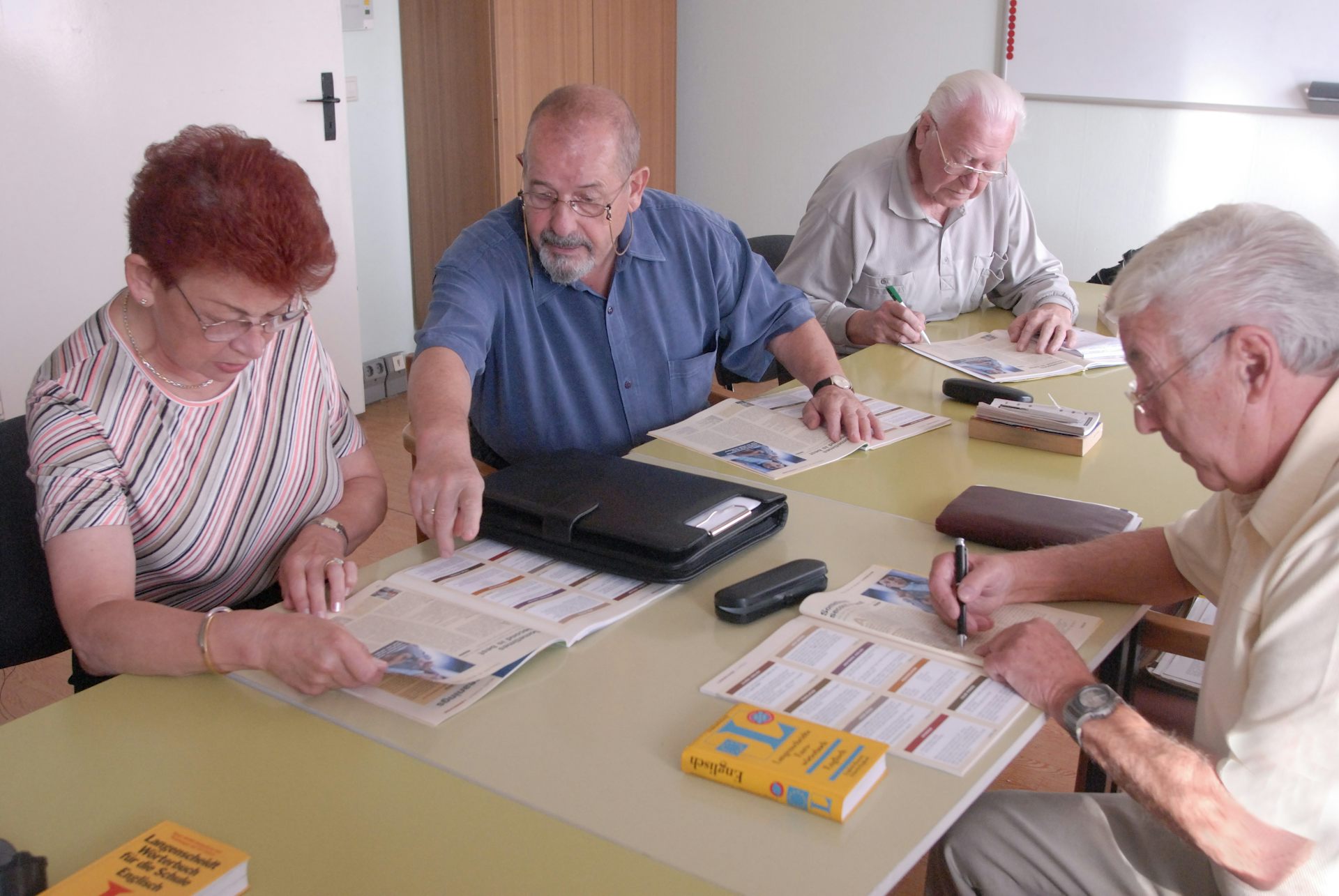 A group of older people sit around a table and look at books.