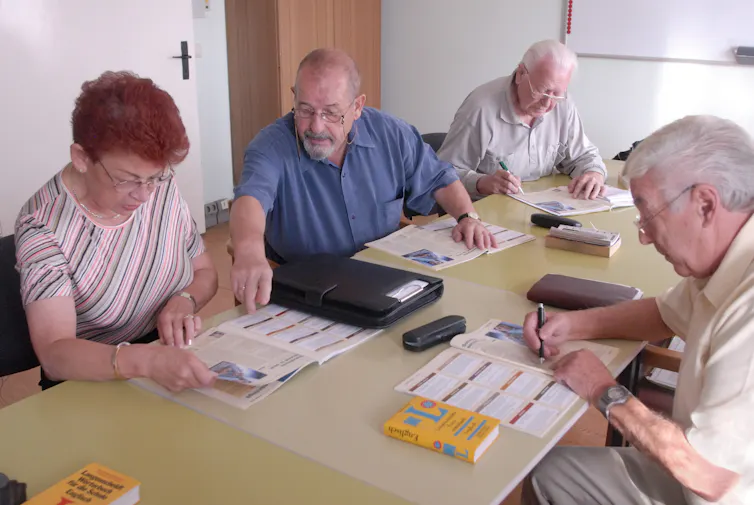 A group of older people sit around a table and look at books.