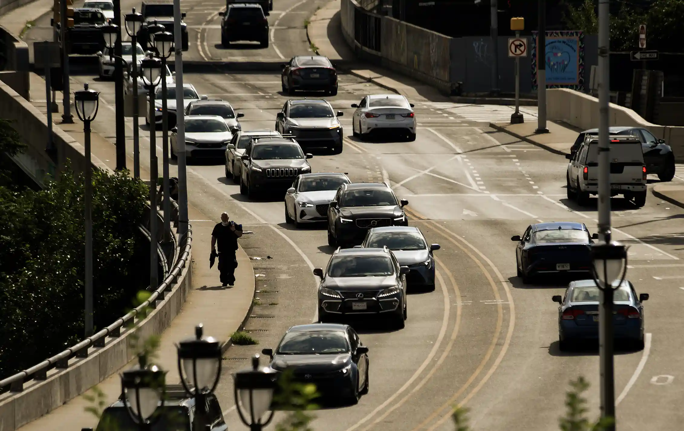 Man walks on sidewalk along traffic on an overpass