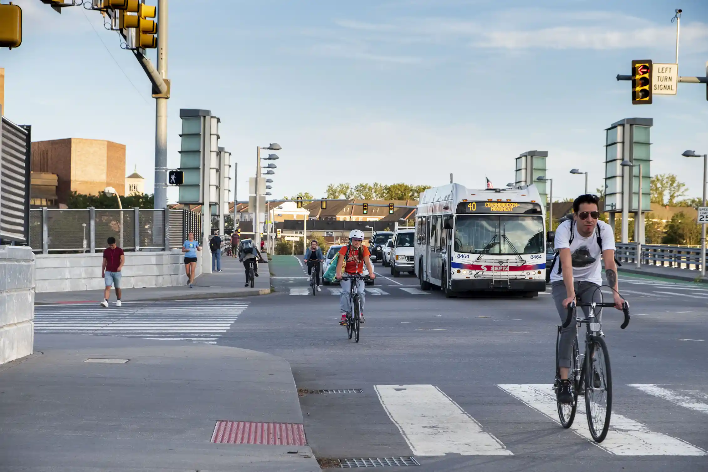 Bicyclists ride down a busy street alongside cars and a bus