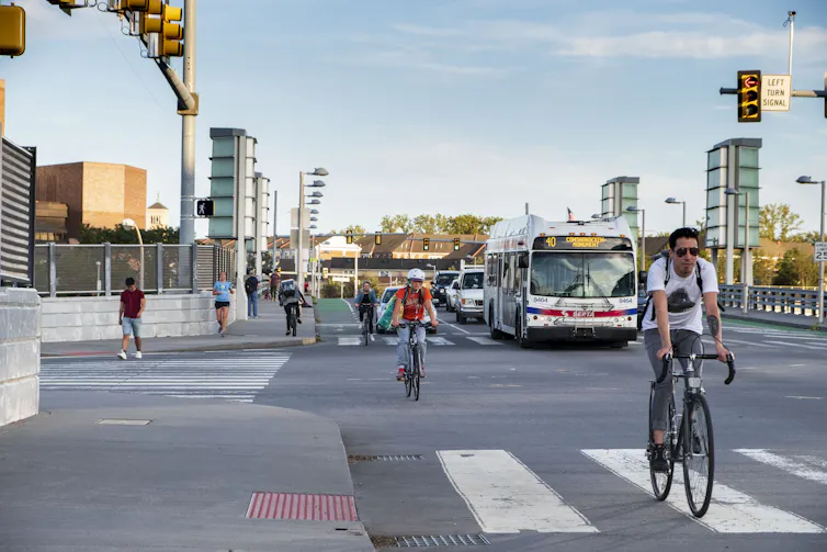 Bicyclists ride down a busy street alongside cars and a bus