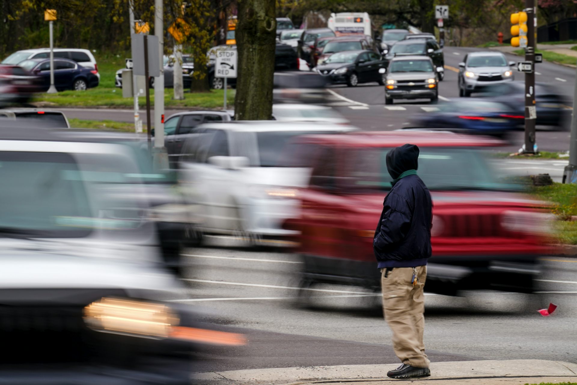 Man waits to cross a busy street filled with moving cars