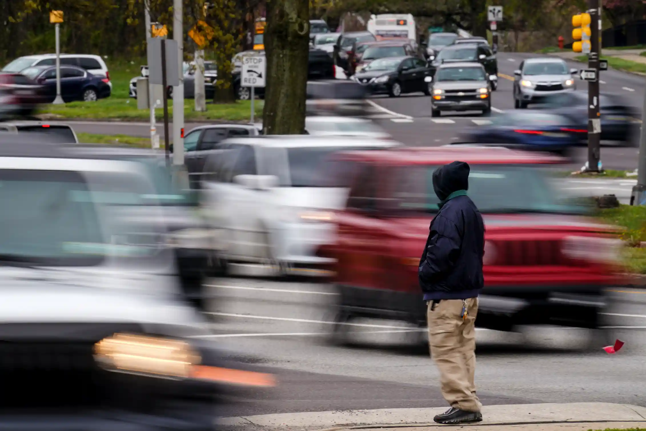 Man waits to cross a busy street filled with moving cars
