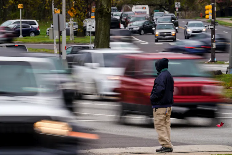 Man waits to cross a busy street filled with moving cars