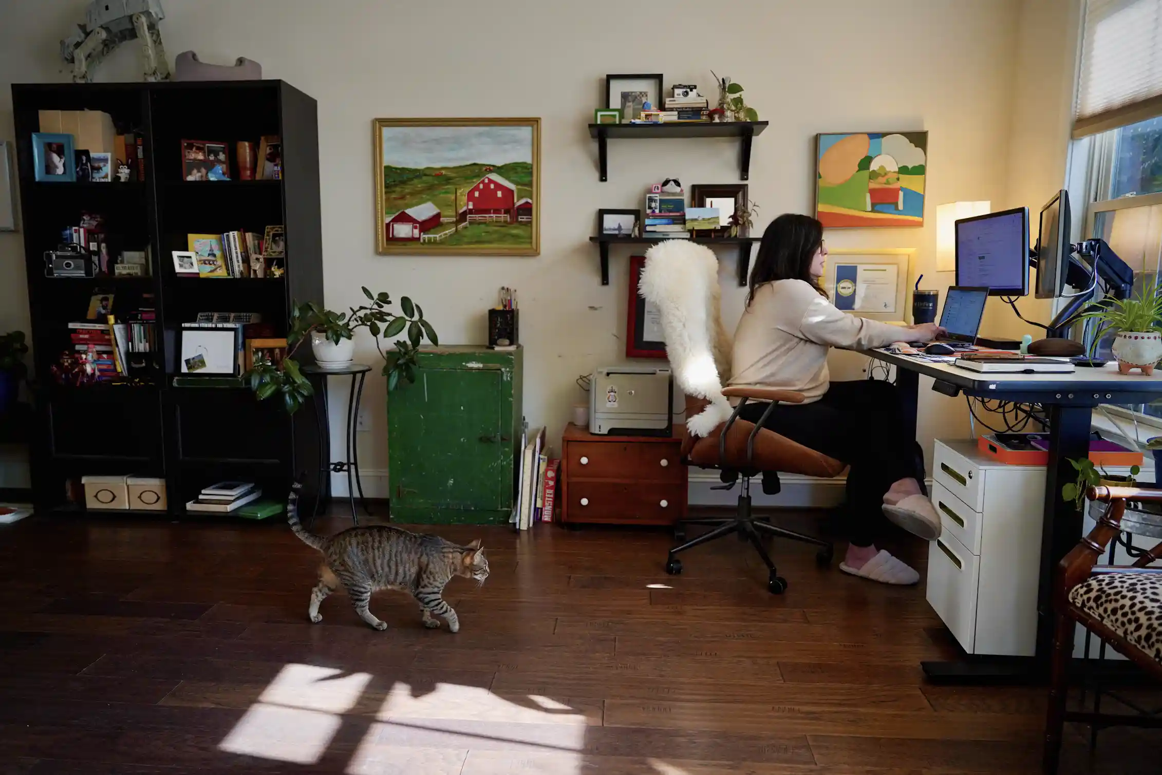 A woman works from home while her cat saunters toward her.