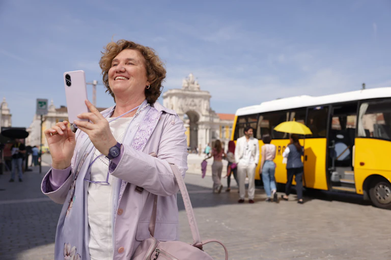 Una mujer saca una foto con un móvil mientras de fondo hay un autobús turístico.
