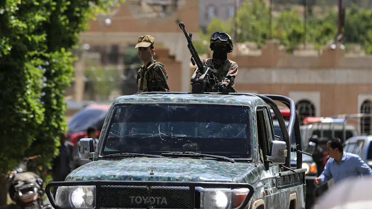 Armed men patrol in an open-top vehicle.
