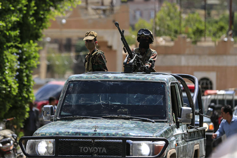 Armed men patrol in an open-top vehicle.