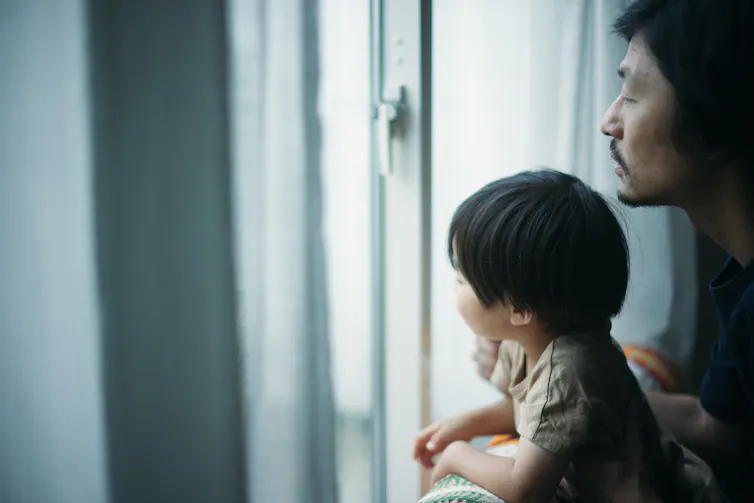 Child looking out of window with adult looking over their shoulder.
