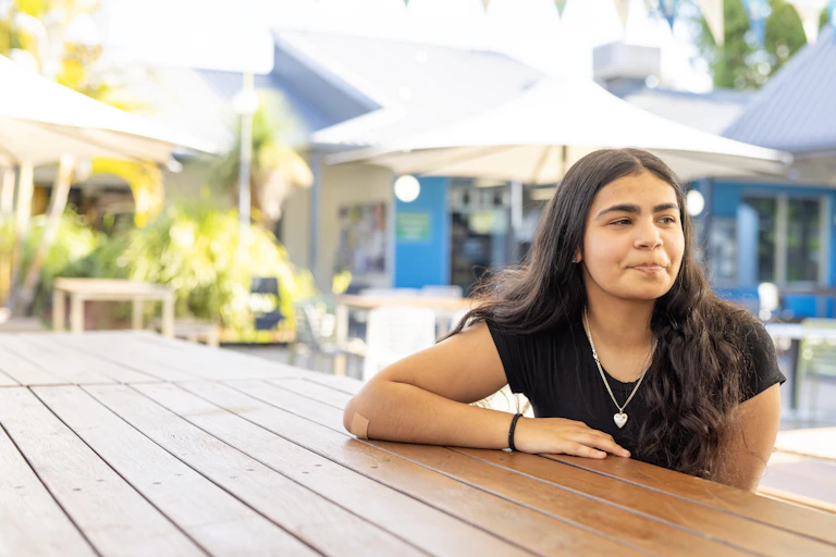 Young Indigenous Australian woman sits at an outdoor cafe.