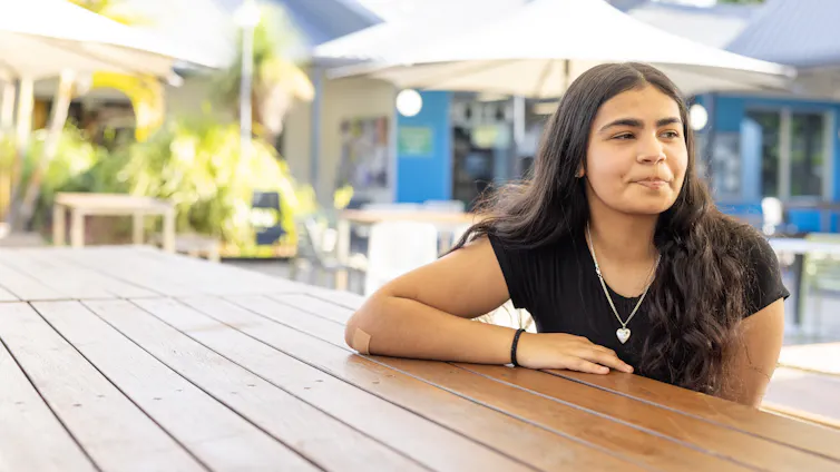 Young Indigenous Australian woman sits at an outdoor cafe.