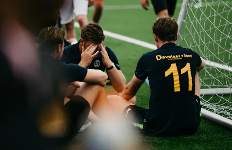 An athlete holds his head in his hands, surrounded by teammates.