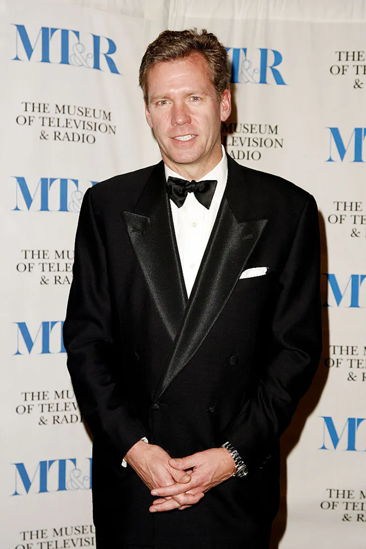 Man wearing a tuxedo poses while clasping his hands at his wasit.