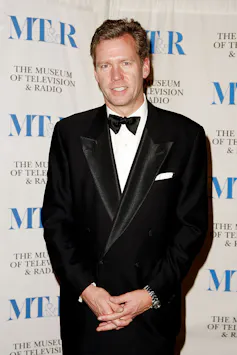Man wearing a tuxedo poses while clasping his hands at his wasit.