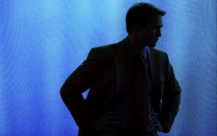 A silhouette of a young man with his hands on his hips against a blue backdrop.
