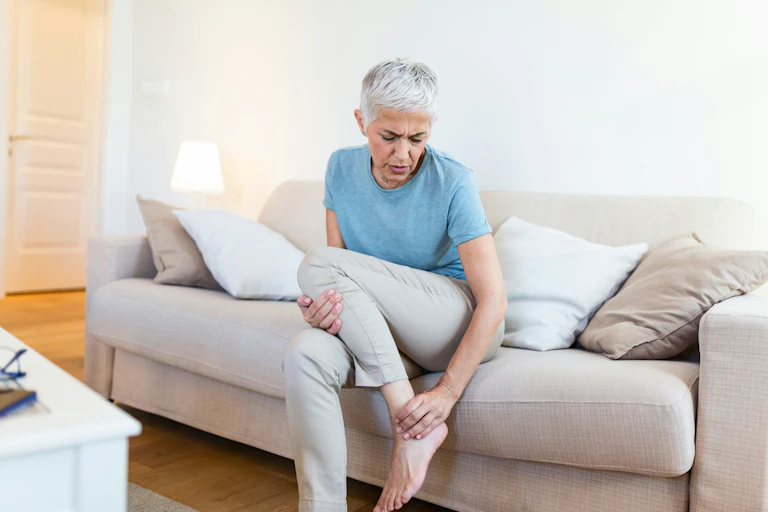 A woman sitting on a sofa rubbing her lower leg