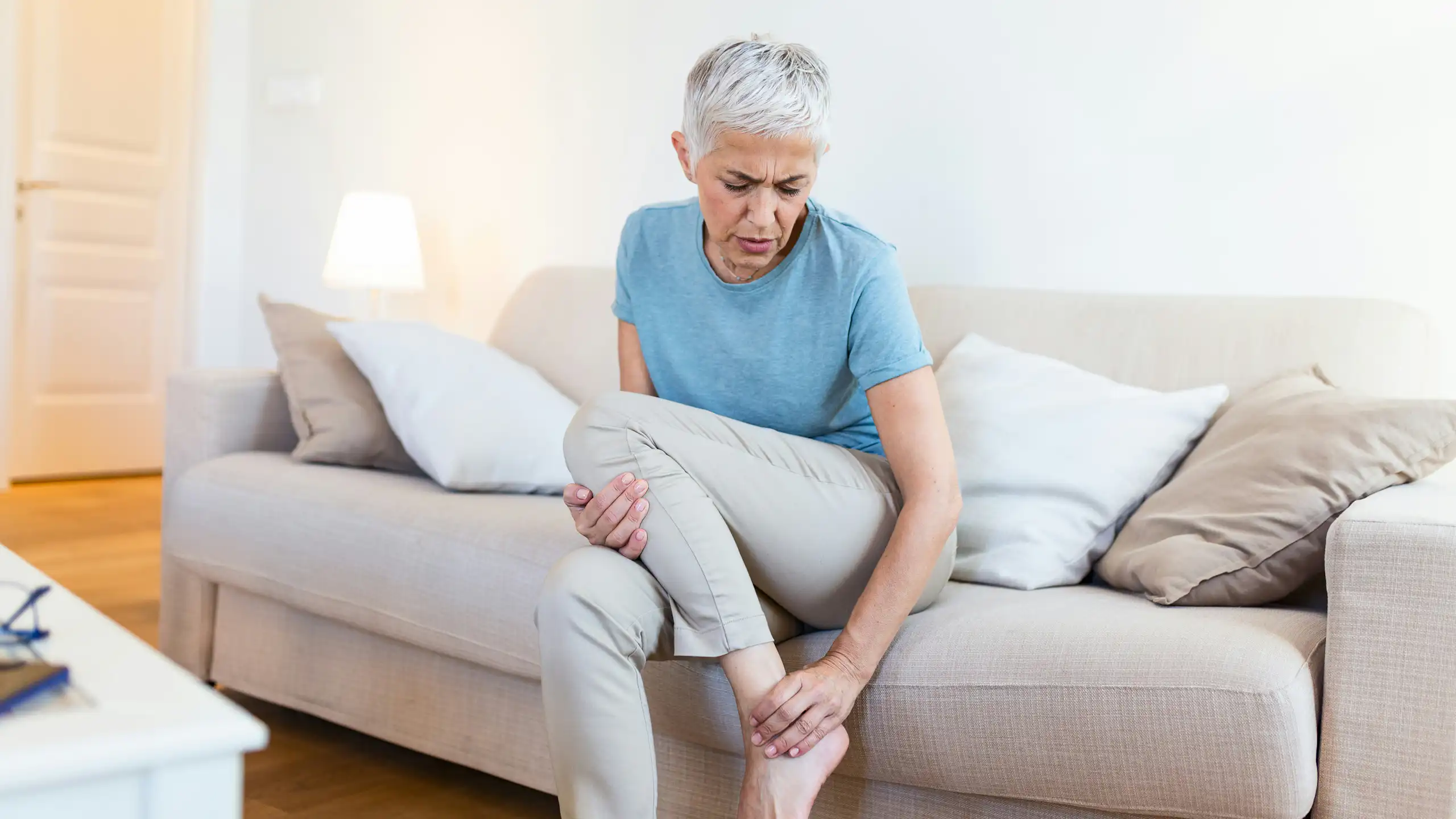 A woman sitting on a sofa rubbing her lower leg
