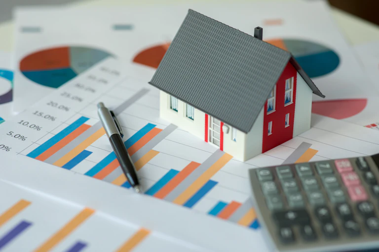 A model home sitting beside a calculator, pen and graphs