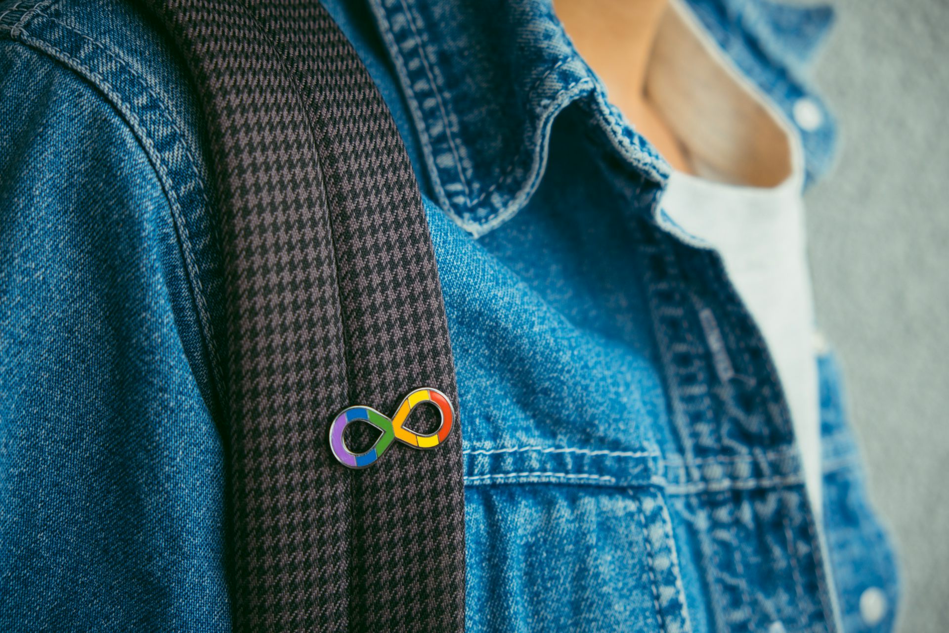 A person wearing an autism infinity symbol rainbow pin on the strap of their backpack.