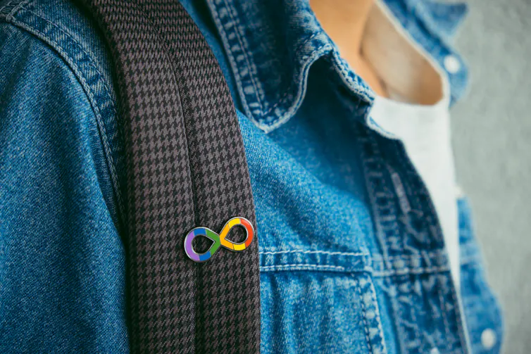 A person wearing an autism infinity symbol rainbow pin on the strap of their backpack.
